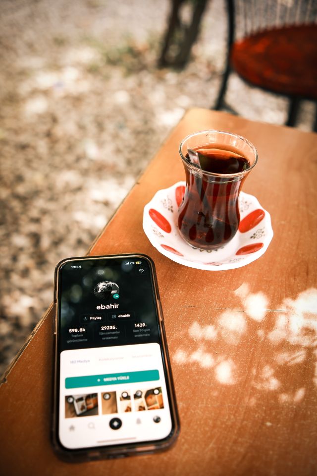 Mobile phone beside traditional Turkish tea on an outdoor wooden table.