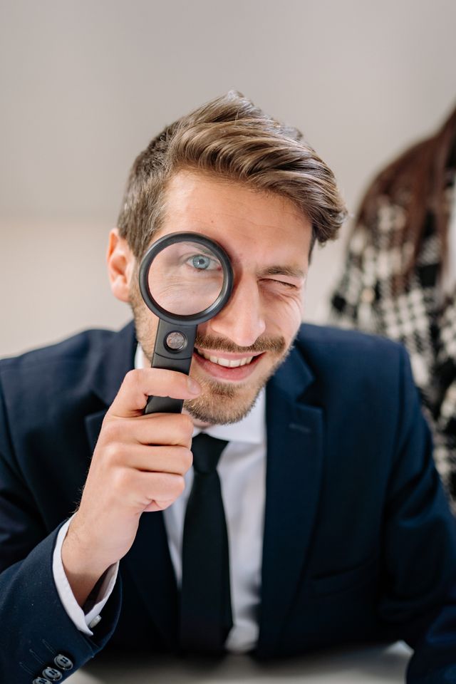 A cheerful businessman in a blue suit holding a magnifying glass to his eye, adding a playful touch.